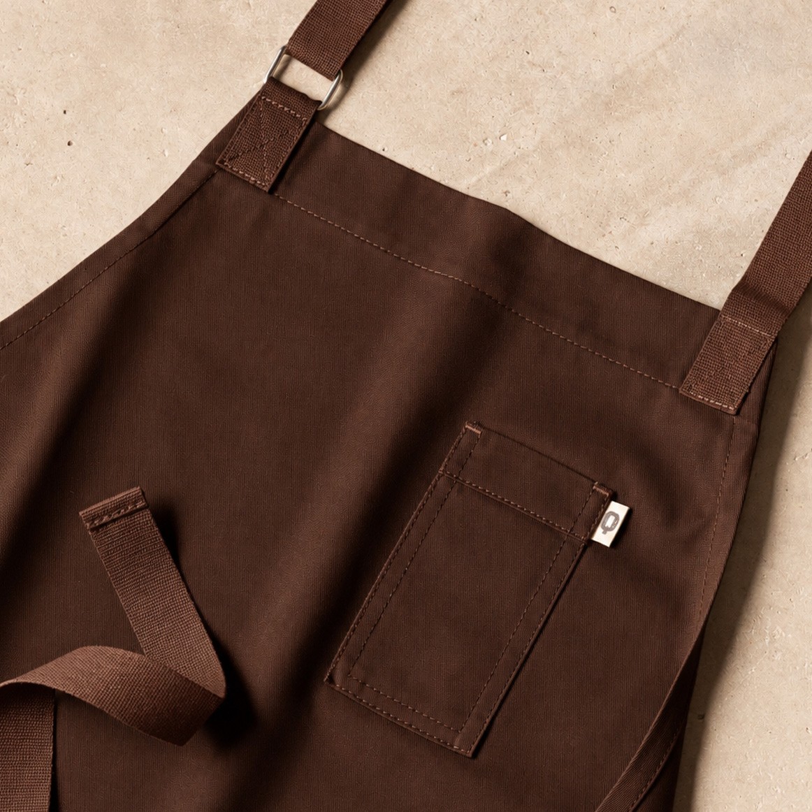 Delantal profesional marrón con bolsillo en el pecho, alternativa al negro en uniformes de hostelería Delantal profesional marrón con bolsillo en el pecho, alternativa al negro en uniformes de hostelería
