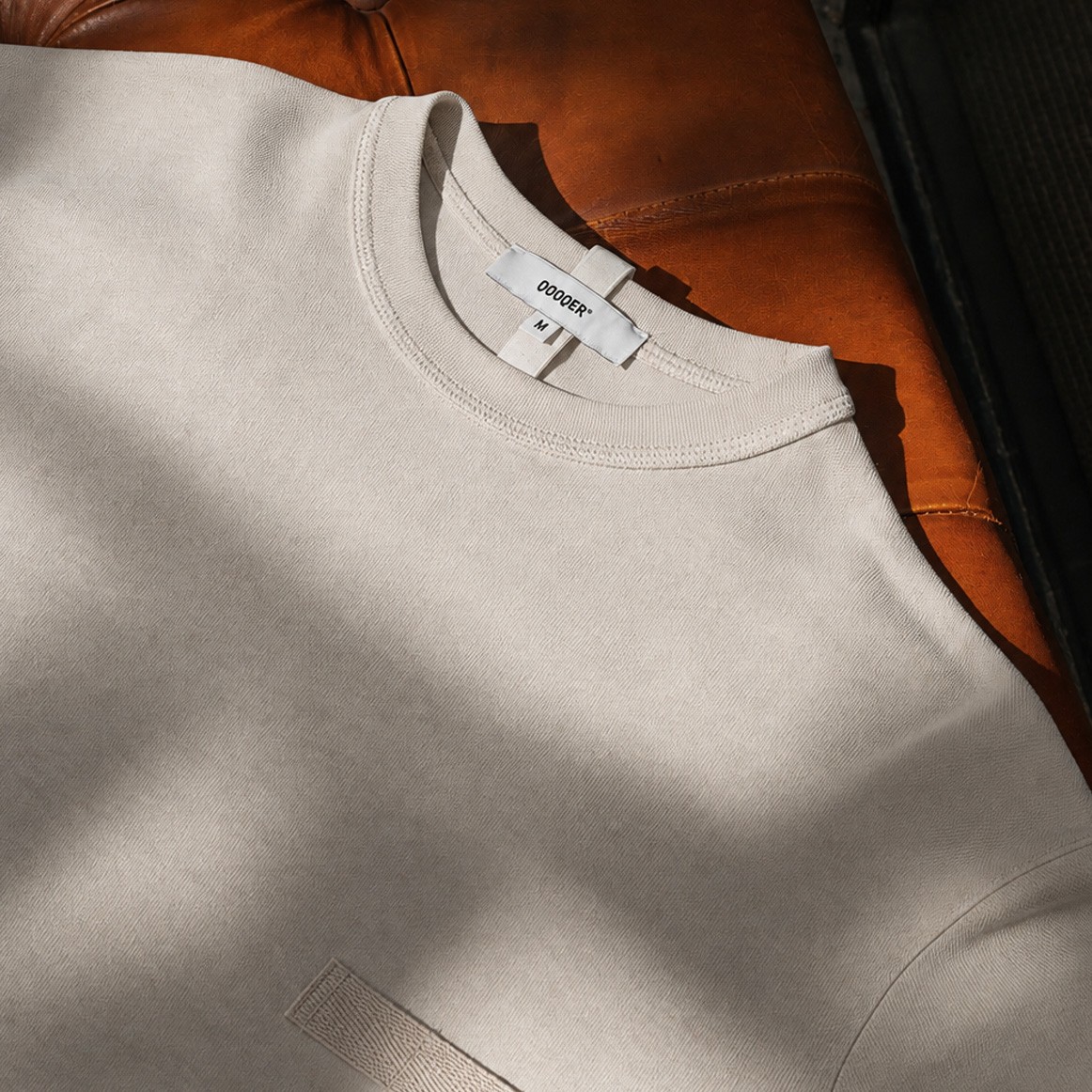 Prenda de uniforme en tono Clay claro sobre sillón de cuero marrón, neutro cálido tendencia 2027 Prenda de uniforme en tono Clay claro sobre sillón de cuero marrón, neutro cálido tendencia 2027